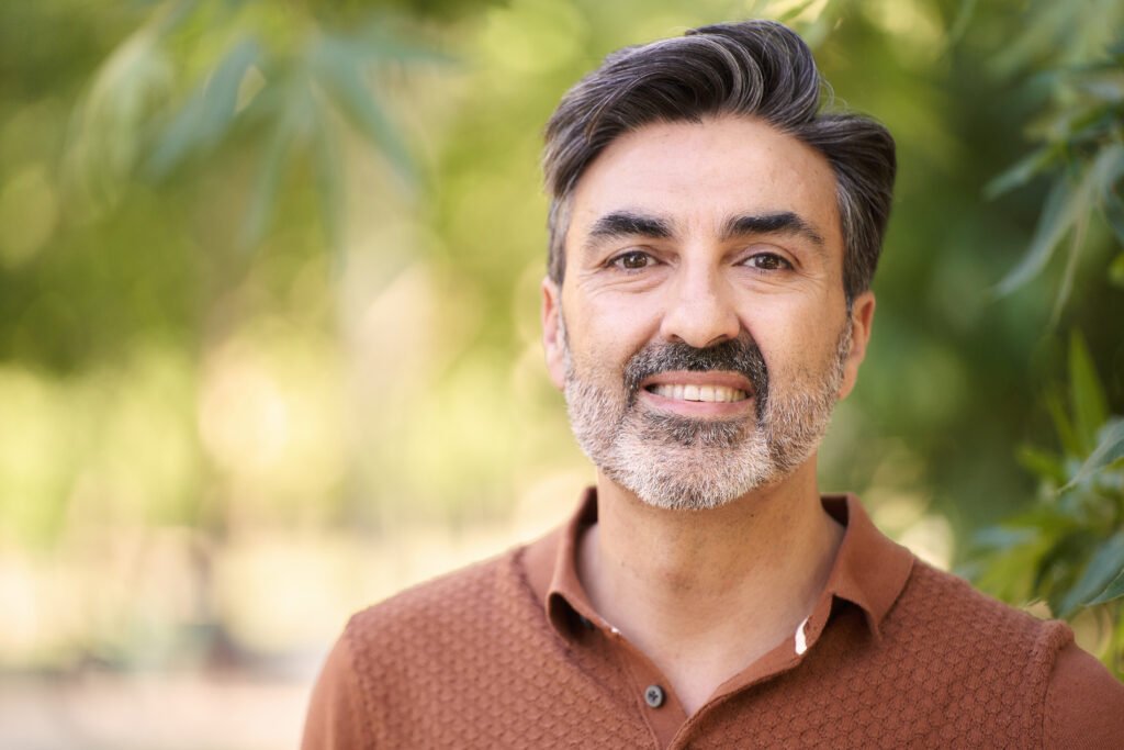 Close-up view of a relaxed middle-aged man looking at camera while standing outdoors in a park.